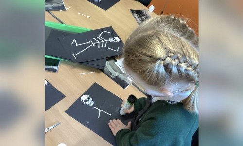A Reception child making a skeleton picture with cotton buds